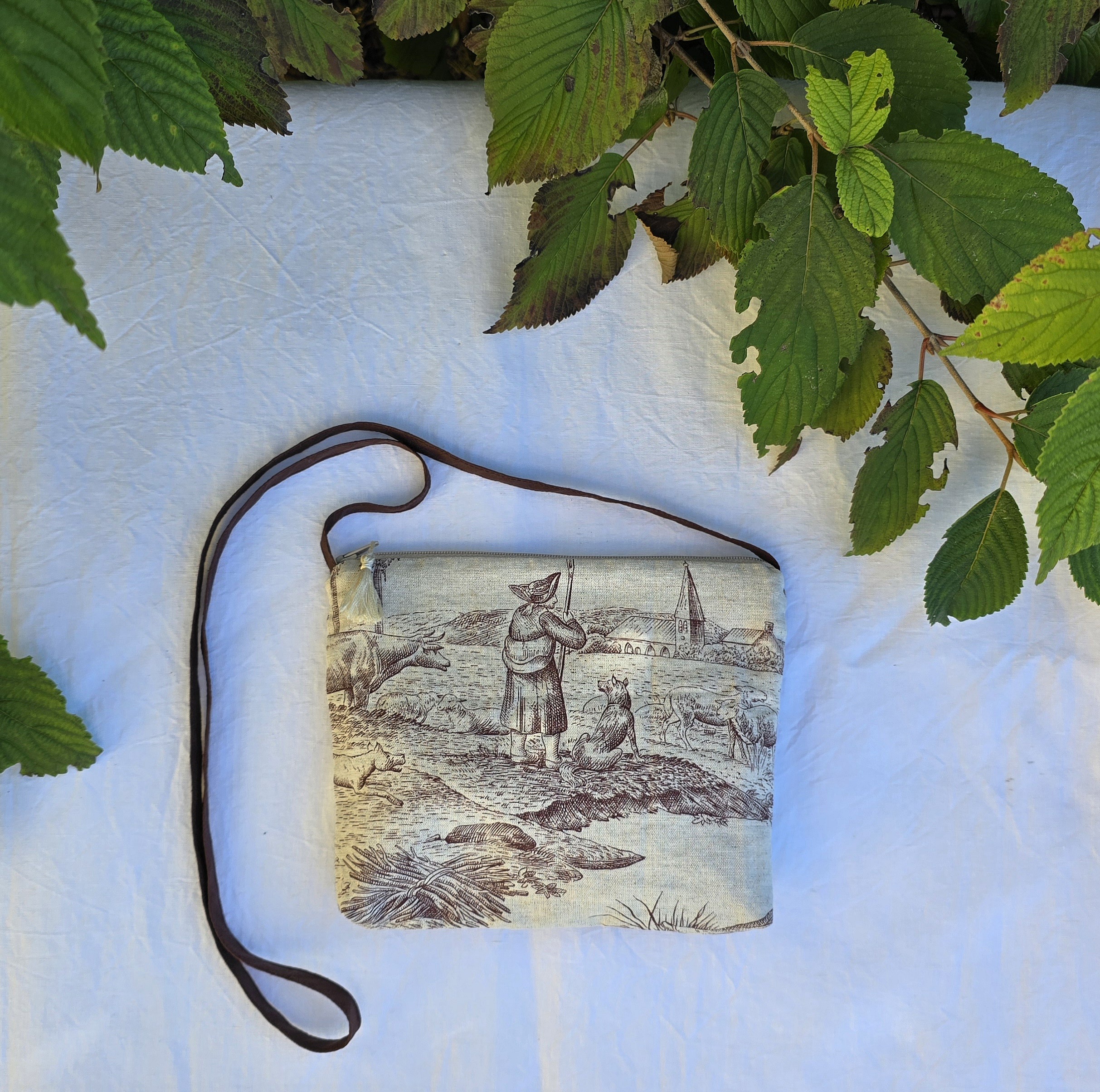 Pochette avec bandouli&egrave;re en tissu toile de Jouy marron et beige agr&eacute;ment&eacute;e d'un pompon