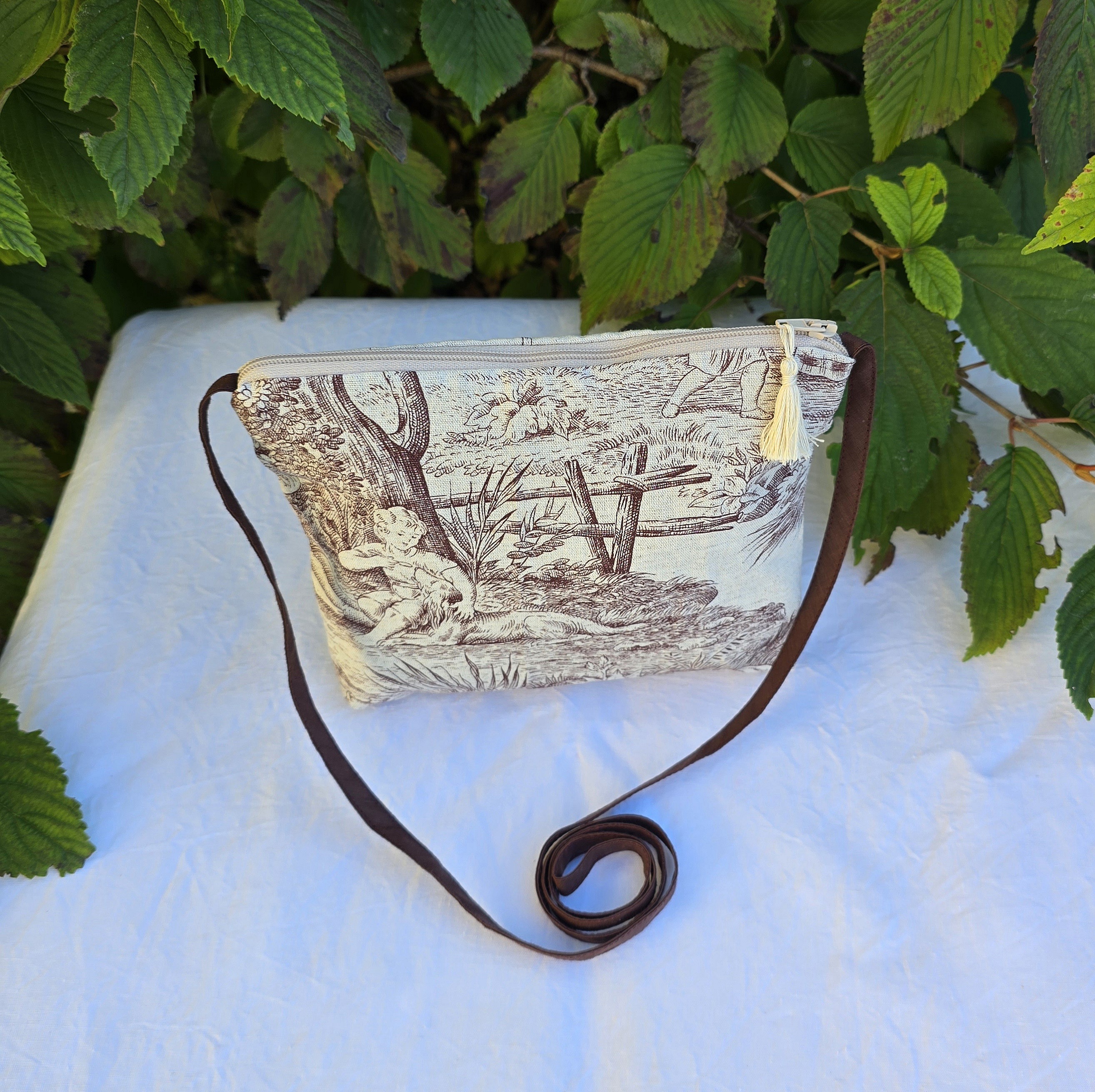 Pochette avec bandouli&egrave;re en tissu toile de Jouy marron et beige agr&eacute;ment&eacute;e d'un pompon