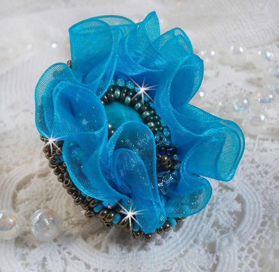 Ilycia sjarmerende ring brodert med en fasettert turkisblå harpiks cabochon og et organzabånd