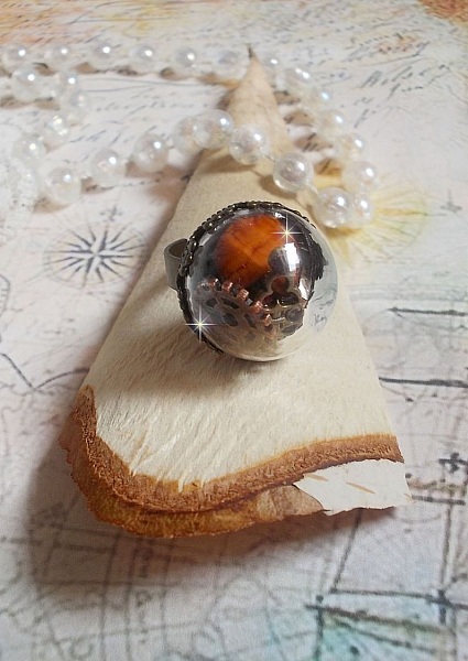Bague Majest&eacute; Steampunk aux rouages m&eacute;caniques &agrave; laquelle s&rsquo;ajoute une cl&eacute; et un strass de couleur Siam et un strass en verre Dor&eacute;. Le tout est mis sous un globe en verre sur une bague r&eacute;glable laiton