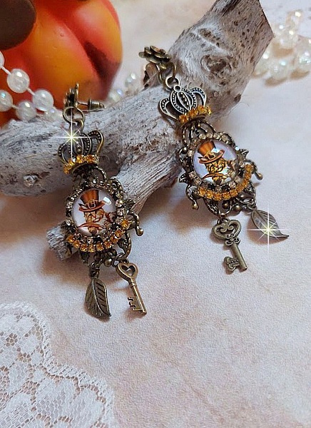 BO Chatibo Steampunk mont&eacute;es avec cabochons ronds en verre repr&eacute;sentant un chat chapeaut&eacute; Haute de Forme Orange. Strass&eacute;es avec une couronne, breloques cl&eacute;s et feuilles. Mont&eacute;es sur clips Bronze