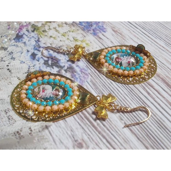 BO Mademoiselle Noellia avec des cabochons ovales repr&eacute;sentant une femme avec un chapeau et un n&oelig;ud blanc &agrave; laquelle s&rsquo;ajoute des cristaux, cha&icirc;nes strass P&ecirc;che et Turquoise sur crochets en plaqu&eacute; Or