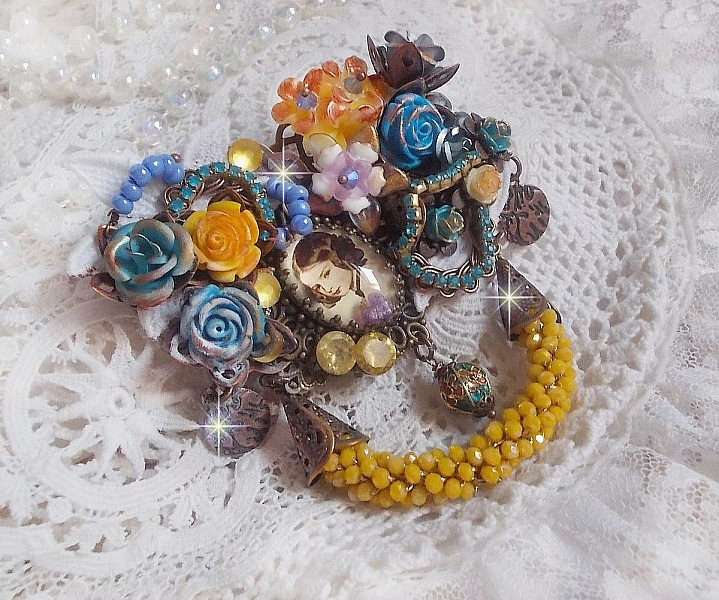 Broche Eclats P&eacute;tillants d&rsquo;inspiration Baroque, orn&eacute;e de fleurs en r&eacute;sine autour d&rsquo;un cabochon strass&eacute;s et perl&eacute;s sur estampes, cristaux, breloques, perle cloisonn&eacute;e, perles jaunes en verre et roses. 