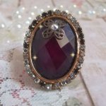Elegant Burgundy-ring laget med PureCrystal-krystaller, et blomsterformet stempel og en glass cabochon.