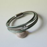 Armbånd i flere skinnfarger i beige, lysegrønne og perlemorfargede nyanser, dekorert med en liten fjær